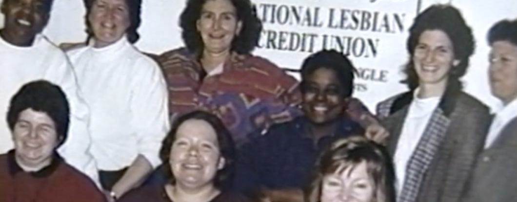 A group of women standing behind a sign that reads 'join to support the first National Lesbian Credit Union'