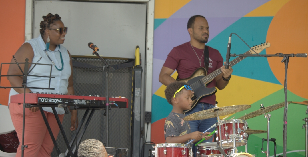 Band playing guitar, drums and keyboard on stage in the day