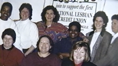 A group of women standing behind a sign that reads 'join to support the first National Lesbian Credit Union'