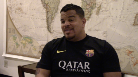 A man sits in front of a world map addressing the camera 