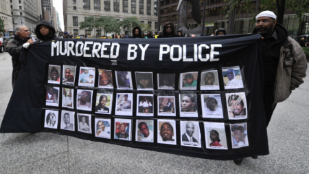 Two people holding a banner showing pictures labeled murdered by police